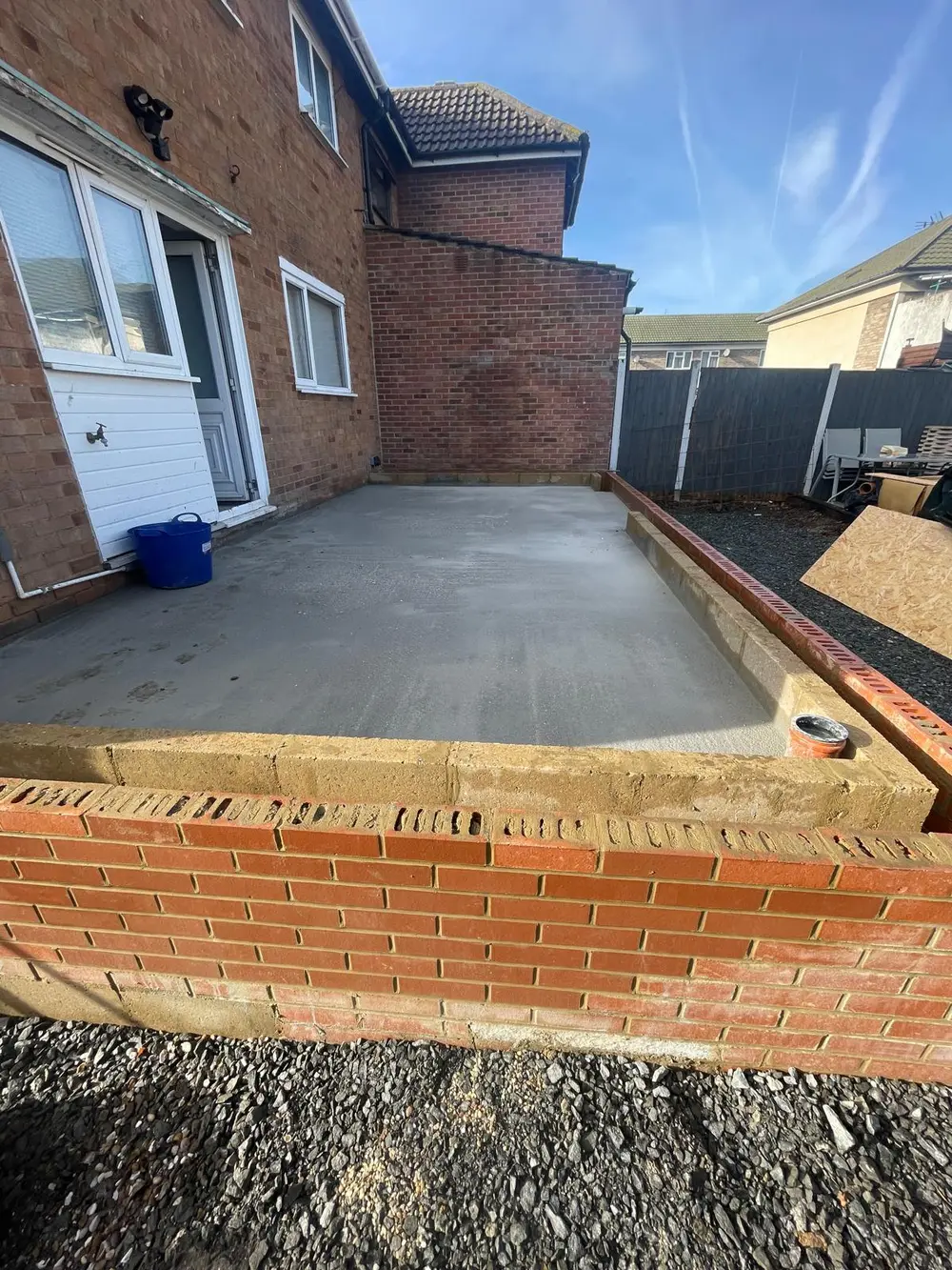 Freshly poured concrete slab and brick footings for a rear extension on a red-brick house